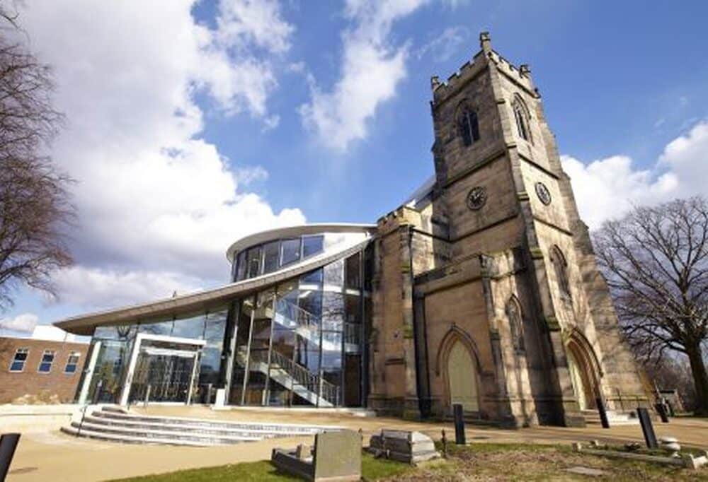 Outside shot of a tall church building with a large glass extension to the left of it.