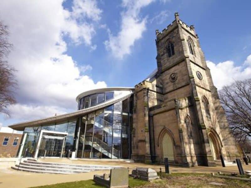 Outside shot of a tall church building with a large glass extension to the left of it.