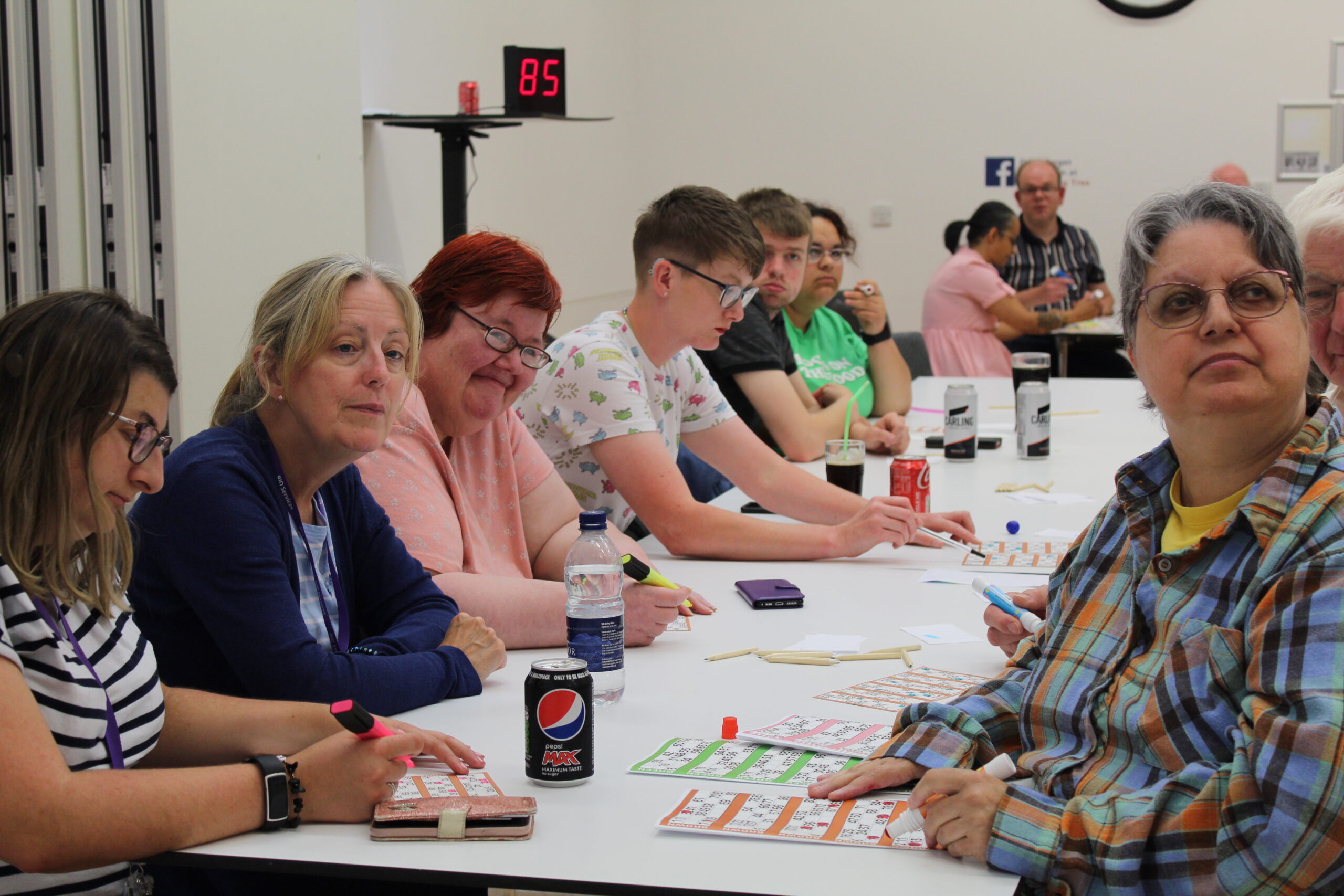 9 men and woman seated at long rectangular tables, looking down at their bingo cards. 